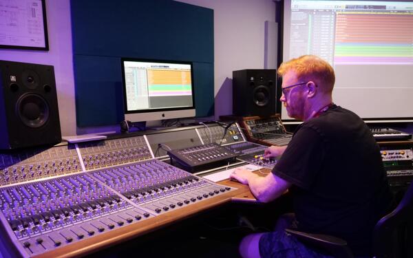 Programme leader sat behind a computer on a DAW with a mixing console around them.