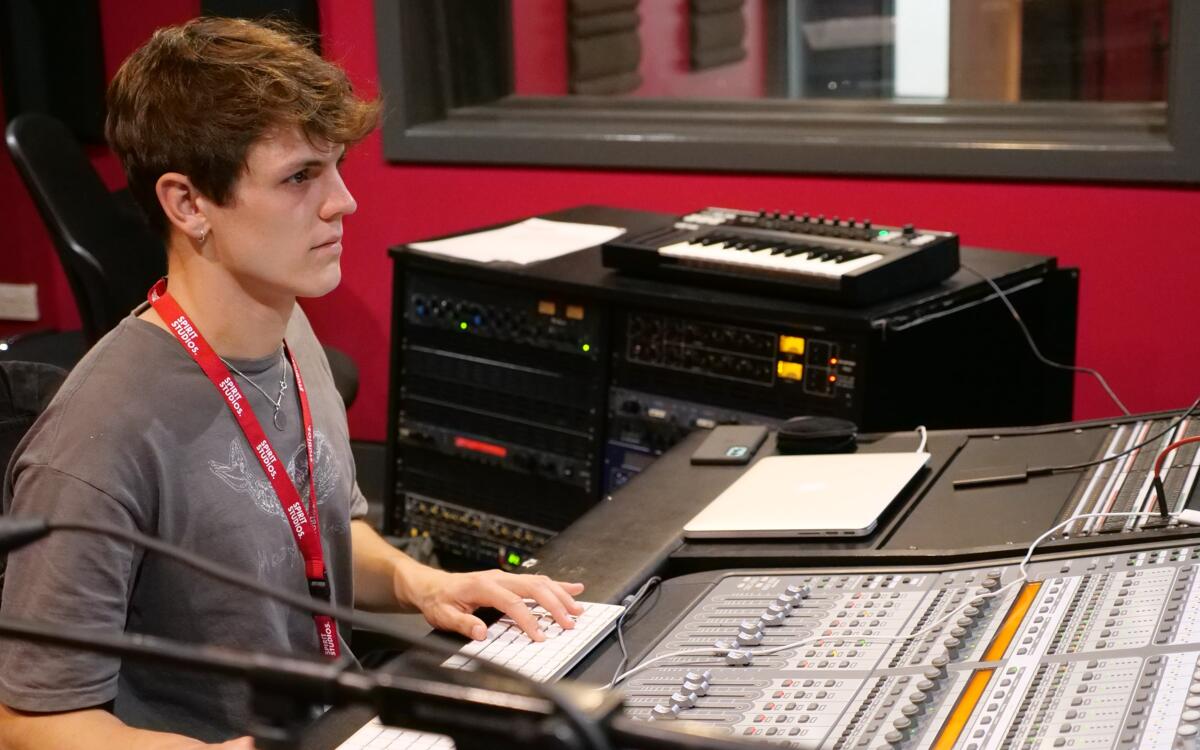 Student in the C24 Studio with a midi controller behind in front of a mixing console