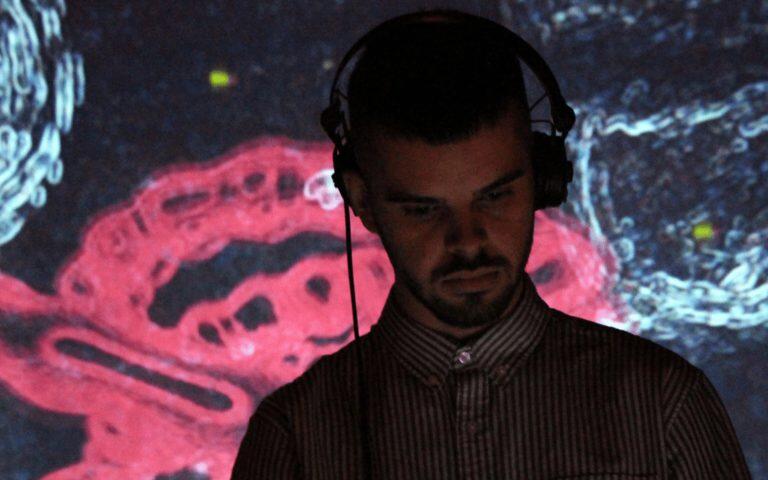 Andy Tomilson (Yant) performing live with headphones on and electronic visuals behind